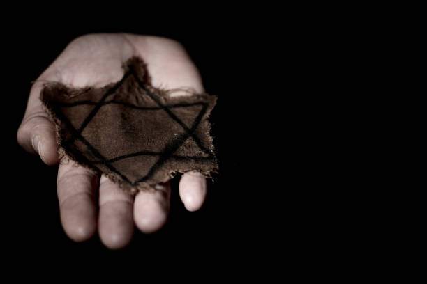 closeup of a ragged Jewish badge in the hand of a man, with a dramatic effect, on a black background with some blank space on the right