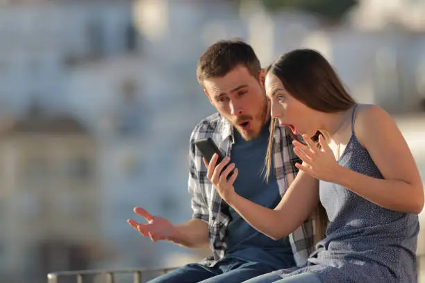 Amazed couple checking smart phone in a town