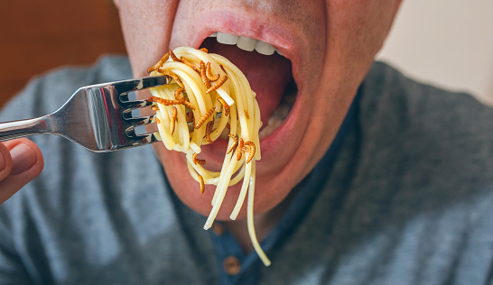Closeup of man eating spaghetti with crispy worms
