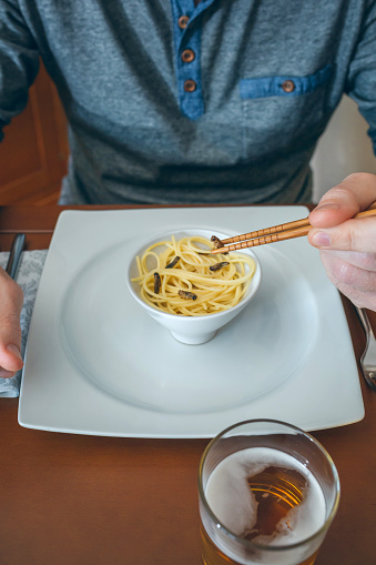 Unrecognizable man eating spaghetti and crickets with chopsticks