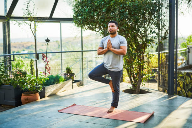 jeune homme pratiquant arbre pose sur le tapis d’exercice - shadow focus on shadow people men photos et images de collection