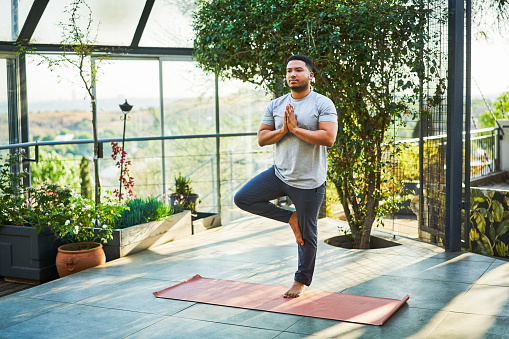 Full length of young man practicing tree pose. Male is exercising on porch. He is in sports clothing.