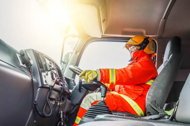 Portrait of confident mature fireman driving firetruck with communication interior view at station