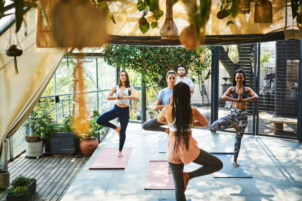 Instructor teaching tree pose to clients on porch Rear view of instructor teaching tree pose to clients on porch. Multi-ethnic people practicing yoga on mat. They are in sports clothing. yoga instructor stock pictures, royalty-free photos & images