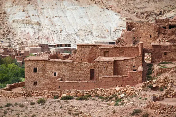 Old Berber village with mud brick architecture in the green oasis of a river valley surrounded by the arid desert landscape of the Atlas Mountains in Morocco
