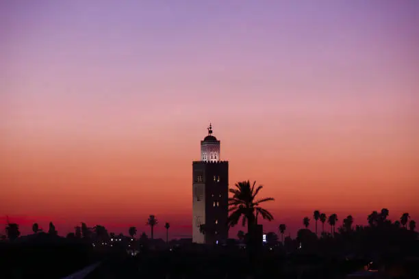 Beautiful sunset in Marrakech, Morocco. Silhouette of oriental architecture minaret tower in front of colorful purple creamy sky