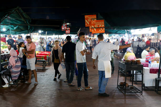 marrakesh, morocco - october 2, 2018: tourists eating together with locals in food stalls in open court market in jemaa el-fnaa square - djemma el fna square imagens e fotografias de stock