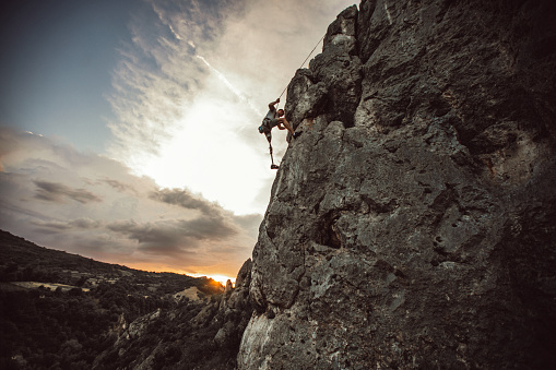 One man, disability young man with prosthetic leg free climbing on a rock mountain in nature..