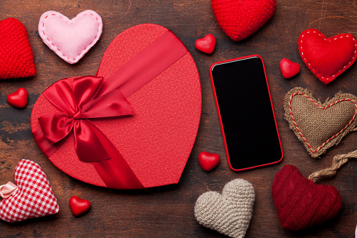 Valentine's day greeting card with knitted hearts, gift box and smartphone on wooden background. Top view with space for your greetings or smart phone app. Flat lay