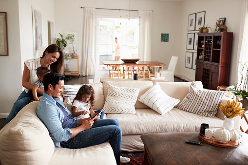 Familia de joven hispana sentada en el sofá leyendo un libro juntos en su sala de estar photo