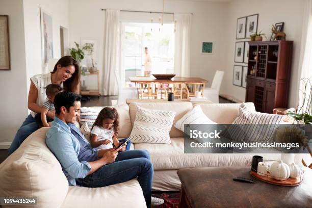 Familia De Joven Hispana Sentada En El Sofá Leyendo Un Libro Juntos En Su Sala De Estar Foto de stock y más banco de imágenes de Familia