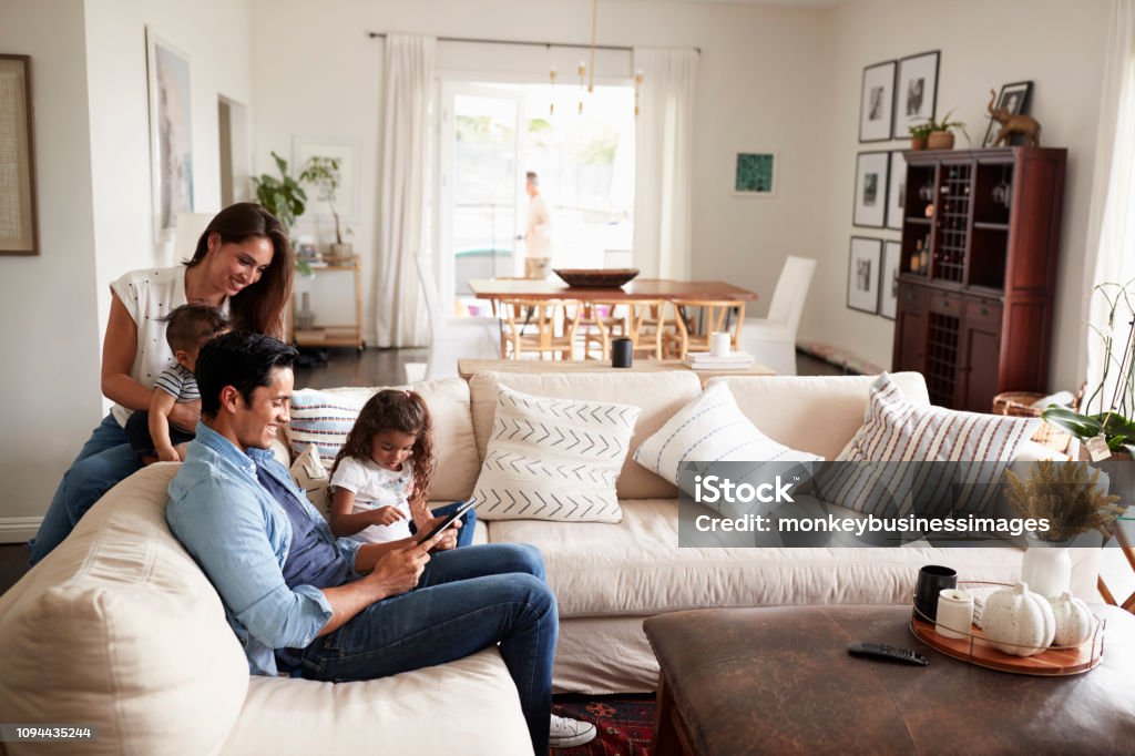 Giovane famiglia ispanica seduta sul divano a leggere un libro insieme nel loro soggiorno - Foto stock royalty-free di Famiglia