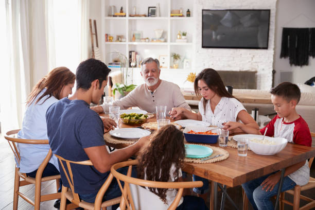 istock Three generation Hispanic family sitting at the table holding hands and saying grace before dinner 1094437270