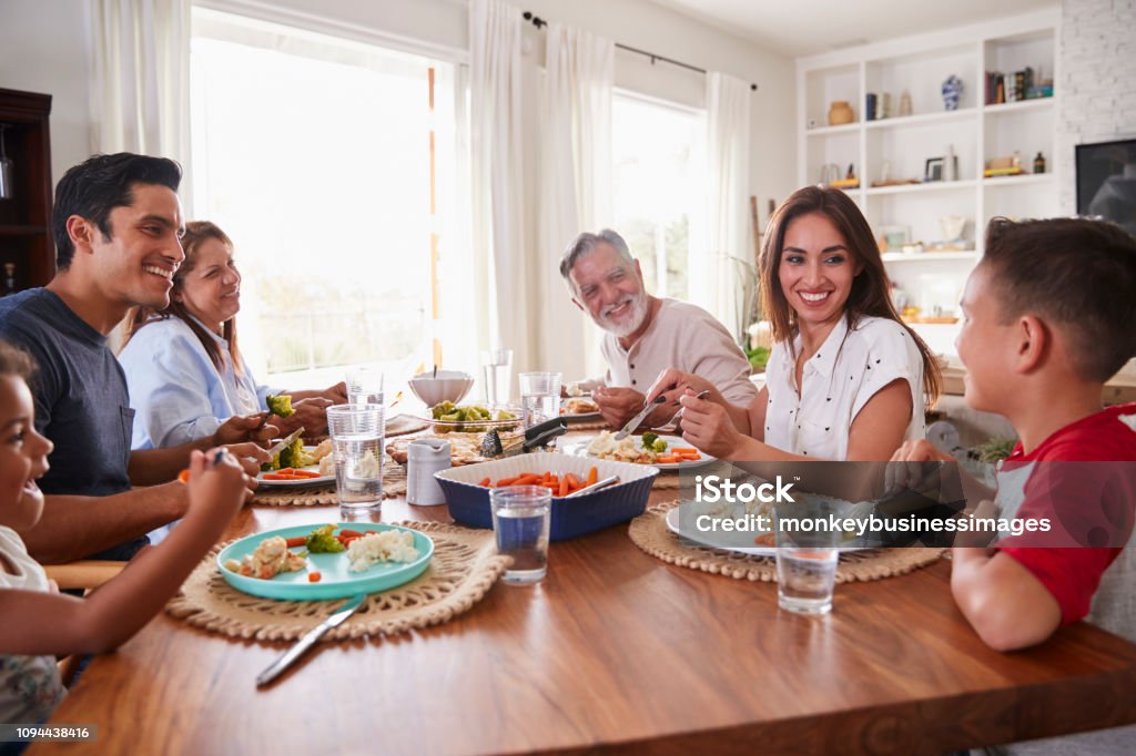 Three generation Hispanic family sitting at the table eating dinner Eating Stock Photo