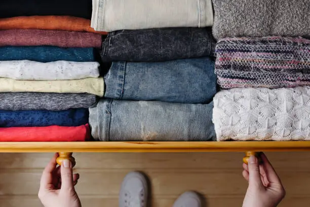 Overhead shot of neatly ordered clothes in wooden drawer. Woman organizing clothes in drawer
