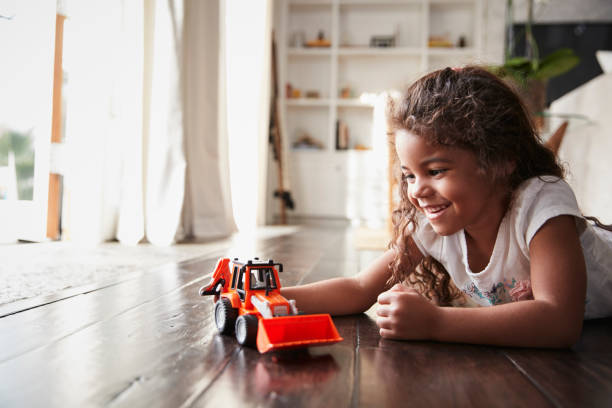 Young Hispanic girl lying on the floor in the sitting room playing with a toy digger truck Young Hispanic girl lying on the floor in the sitting room playing with a toy digger truck gender neutral photos stock pictures, royalty-free photos & images