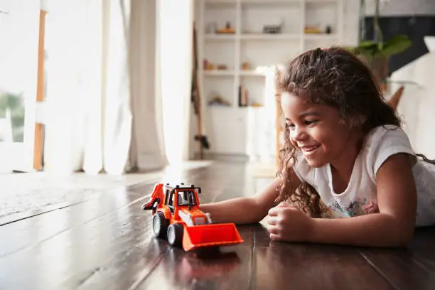 Photo of Young Hispanic girl lying on the floor in the sitting room playing with a toy digger truck