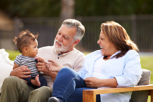 senior couple sitting in the garden with their baby grandson, smiling at him, front view - grandparent grandfather grandmother child imagens e fotografias de stock