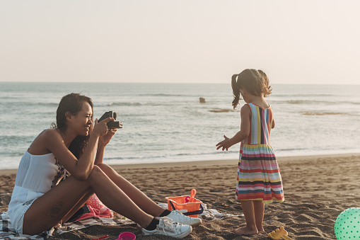 Mother photographing little daughter at the beach with instant camera
