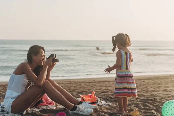 Photo of Mother photographing daughter at the beach with instant camera