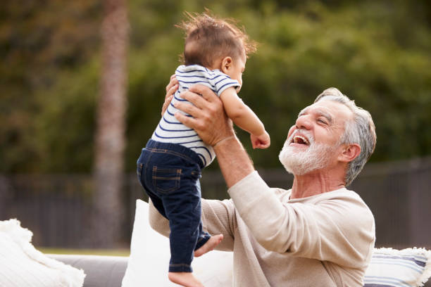 Senior Hispanic man sitting in the garden lifting his baby grandson in the air and smiling to him Senior Hispanic man sitting in the garden lifting his baby grandson in the air and smiling to him grandfather stock pictures, royalty-free photos & images