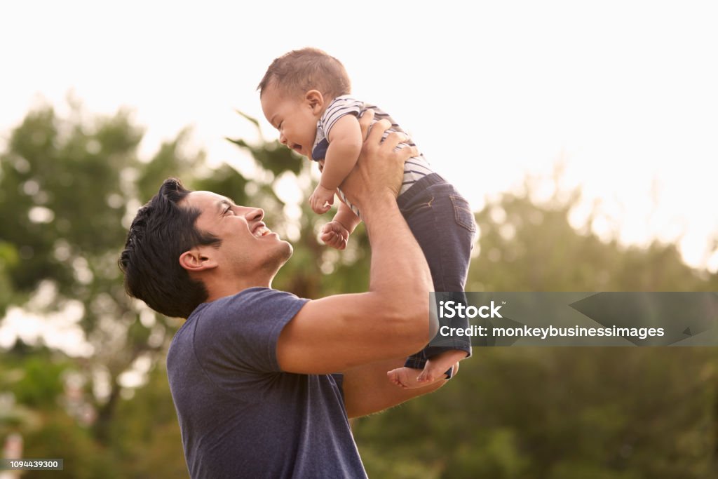 Millennial Hispanic father holding his little baby in the air in the park, close up Father Stock Photo