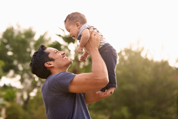 Millennial Hispanic father holding his little baby in the air in the park, close up Millennial Hispanic father holding his little baby in the air in the park, close up father and baby stock pictures, royalty-free photos & images