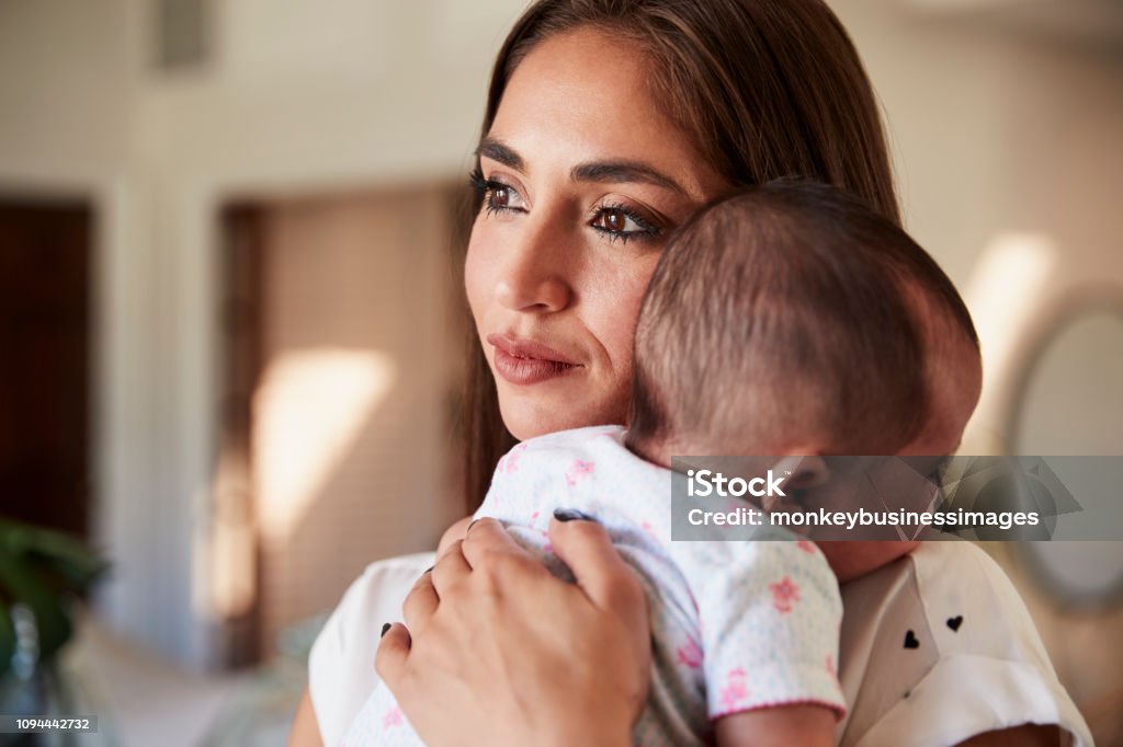 Millennial Hispanic mother holding her newborn son close to her chest, head and shoulders, close up Mother Stock Photo