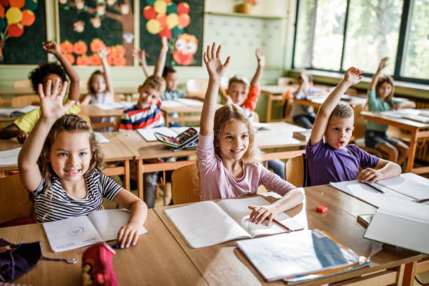 istock Happy school children raising their arms to answer the question on a class. 1094443154