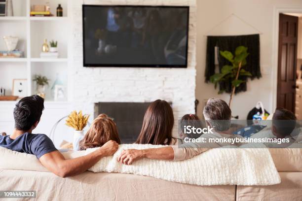 Vista Posteriore Della Famiglia Ispanica Di Tre Generazioni Seduta Sul Divano A Guardare La Tv - Fotografie stock e altre immagini di Guardare la TV