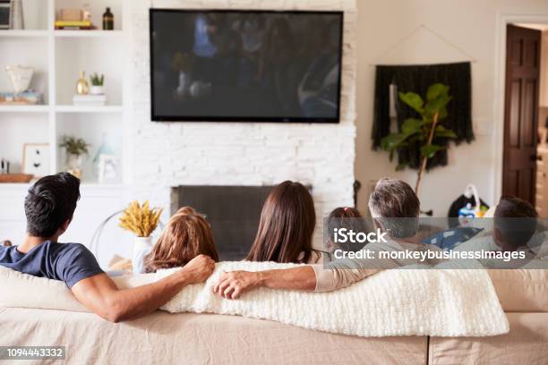 Back View Of Three Generation Hispanic Family Sitting On The Sofa Watching Tv Stock Photo - Download Image Now