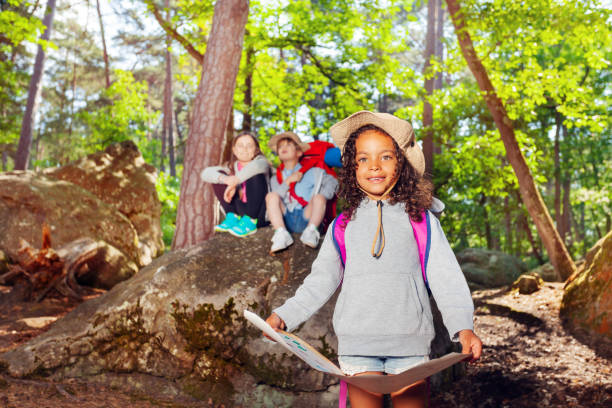 Girl with map and other scout kids in the forest learning orientation during summer holidays camping