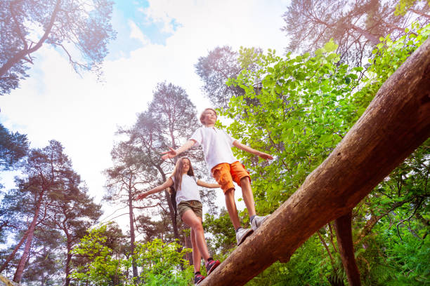 istock Boy and girl walks over the high log in forest 1094443694