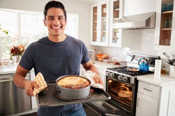 millénaire hispanique homme debout dans la cuisine présentant le gâteau souriant il a cuit à la caméra - home baking photos et images de collection