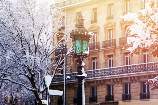 Close-up picture of old snow covered lamp post on the winter cityscape background, Paris, France