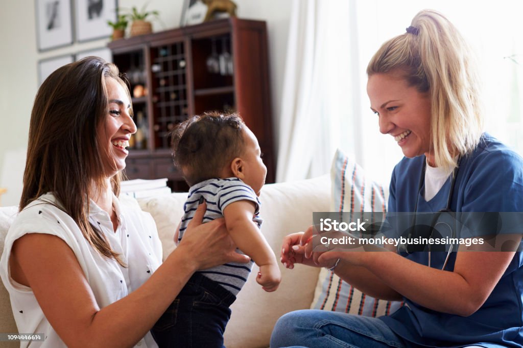 Female healthcare worker visiting a young mum and her infant son at home Nurse Stock Photo