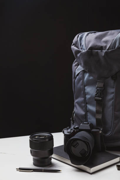 istock backpack, photo camera with lens and notebook with pen on black 1094448868