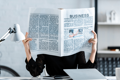 businesswoman reading newspaper and hiding face