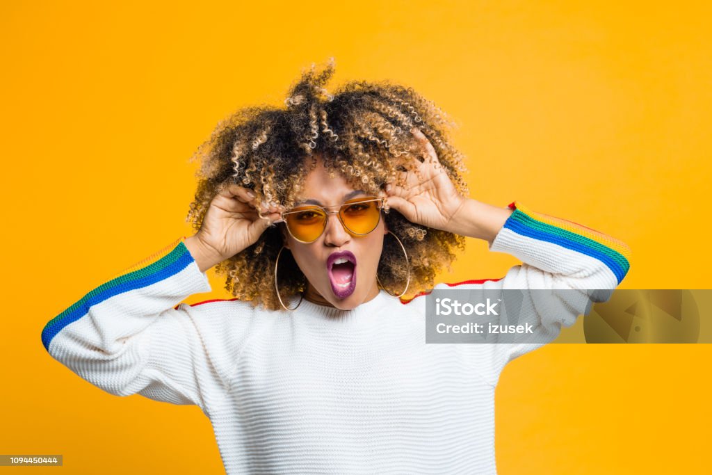 Funky afro girl against yellow background Beautiful and energetic afro young woman screaming at camera against yellow background. Studio shot. Afro Hairstyle Stock Photo