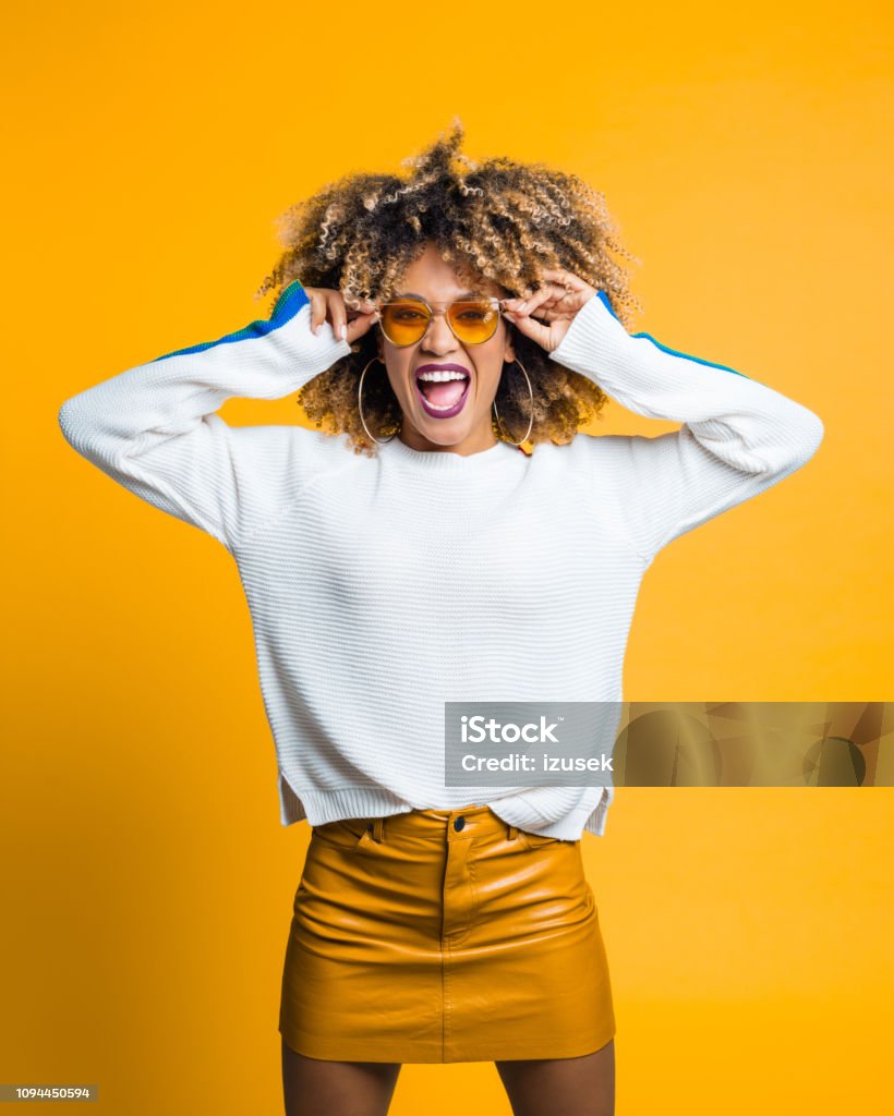 Funky afro young woman against yellow background Beautiful and energetic afro young woman screaming at camera against yellow background. Studio shot. Colored Background Stock Photo