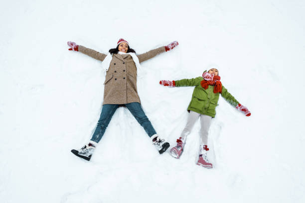 attractive african american mother and cute daughter doing snow angels in winter forest attractive african american mother and cute daughter doing snow angels in winter forest snow angels stock pictures, royalty-free photos & images