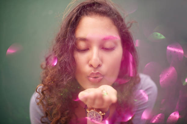 Studio shot of an attractive young woman blowing pink powder against a grey background