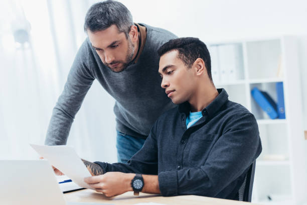 istock bearded mentor looking at young colleague working with papers in office 1094462952