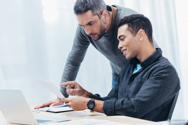 istock smiling young businessman pointing with finger at papers while working with colleague in office 1094462974