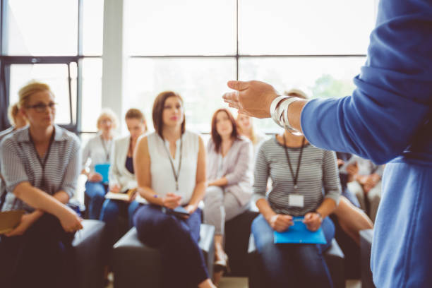 Speaker addressing group of females Hand of a trainer addressing group of females sitting in a conference hall. Female hand against defocused group of women attending seminar. training course stock pictures, royalty-free photos & images