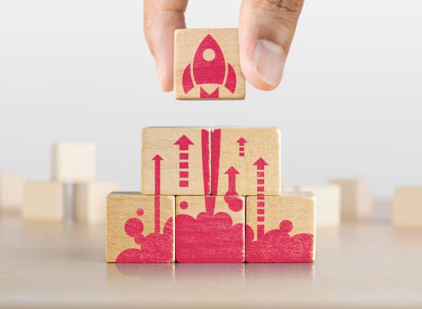 Business start up, start, new project or new idea concept. Wooden blocks with launching rocket graphic arranged in pyramid shape and a man is holding the top one. stock photo