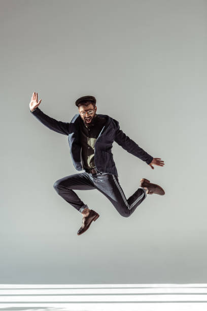 istock handsome man in cap and glasses jumping on grey background 1094470056