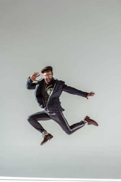 istock handsome man in cap and glasses jumping on grey background 1094470062