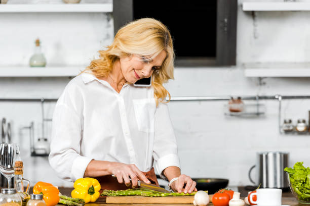 istock attractive middle aged woman talking by smartphone while cooking in kitchen 1094473280