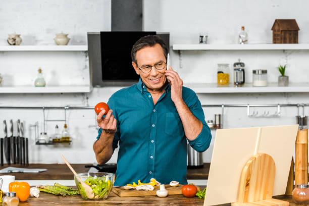 istock handsome mature man talking by smartphone while cooking in kitchen 1094473794